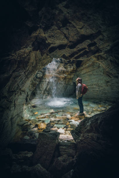 istock Woman standing in cave and looking at waterfall 1214094730