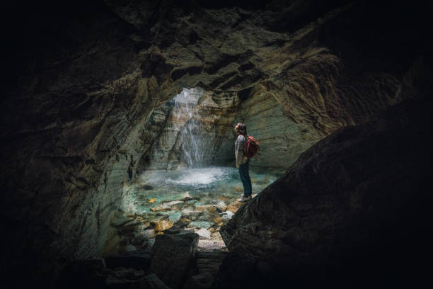 istock Woman standing in cave and looking at waterfall 1214094731
