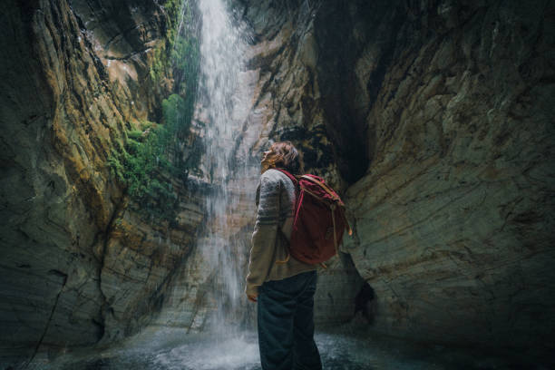 istock Woman standing in cave and looking at waterfall 1214095482