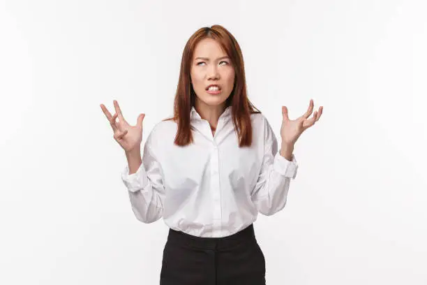 Pissed-off asian woman hates annoying clients. Distressed and tensed irritated female in white shirt, squeez hands in fists losing patience looking up, boiling from annoyance, white background.