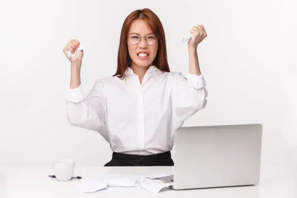 Career, work and women entrepreneurs concept. Close-up portrait of pissed-off bothered asian office lady, manager hate paperwork, squeeze documents from anger and annoyance, sit near laptop.