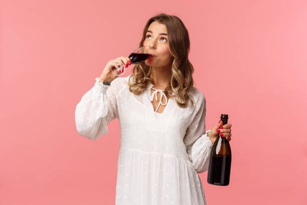 Holidays, spring and party concept. Portrait of young elegant happy blond woman, wear white trendy dress, drinking wine from glass looking up pleased, tasting good drink, hold bottle Holidays, spring and party concept. Portrait of young elegant happy blond woman, wear white trendy dress, drinking wine from glass looking up pleased, tasting good drink, hold bottle. cake models stock pictures, royalty-free photos & images