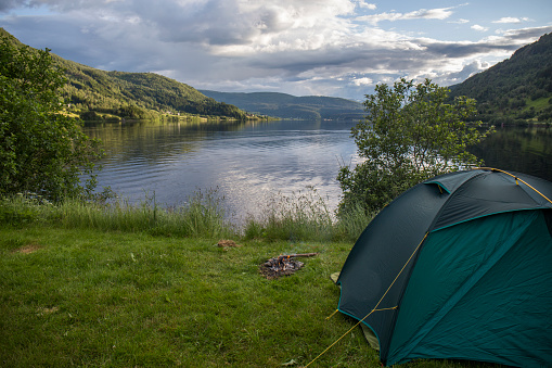 free camping in spectacular scenery, green tent, camping equipment, abundant green vegetation, nordic fjord, blue water, summer days in Norway