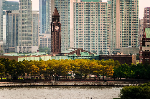 A view of Jersey City from Castle Point in Hoboken New Jersey. The Hoboken Train Station is in the foreground with its tall clock tower with the caption of the EXTINCT Erie Lackawanna Railroad system. In the foreground is a cove of the Hudson that separates New Jersey from New York City. Jersey City is a suburban city across the Hudson River from Downtown New York City and is home to many New Jersey residents that work in New York City.