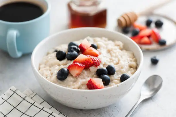 Photo of Oatmeal porridge with berries, honey and cup of coffee