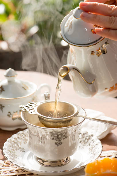 thé noir chaud étant versé par la passoire antique de thé argentée dans la tasse de thé anglaise sur la table de thé d’après-midi - tea cup afternoon tea tea teapot photos et images de collection