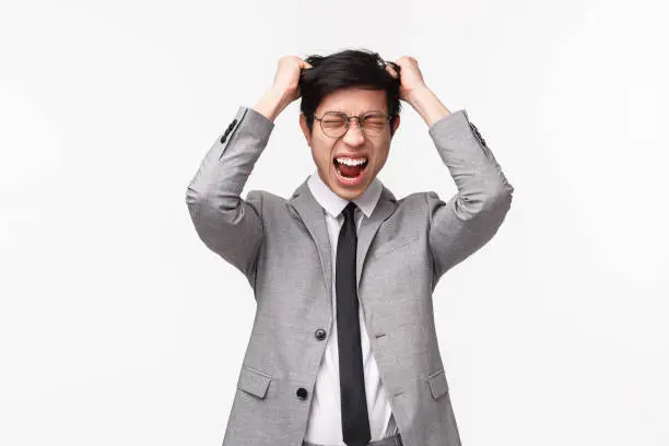 Depression, people and emotion concept. Waist-up portrait of tensed and stressed-out asian young man in formal suit, tie, pull hair from head and scream upset, standing white background.