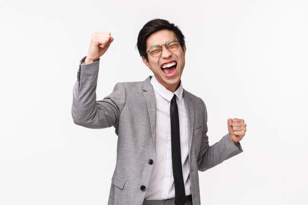 retrato de cintura arriba de un joven hombre de negocios asiático aliviado y exitoso, empresario masculino en traje gris, bomba de puño, baile de campeón, gritando sí victoria, triunfando sobre el logro, ganando - waistup fotografías e imágenes de stock