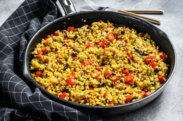 Cooked bulgur with vegetables in a pan. Gray background. Top view