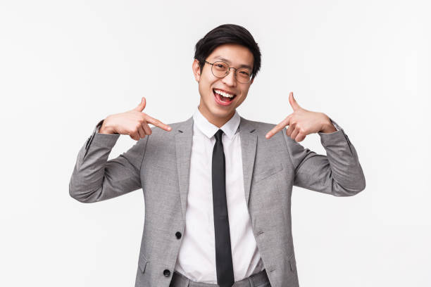 retrato de cintura arriba de un joven y exitoso hombre de negocios asiático presumiendo de su propio logro, logro personal, sonriendo y señalándose, de pie en el fondo blanco de traje - waistup fotografías e imágenes de stock
