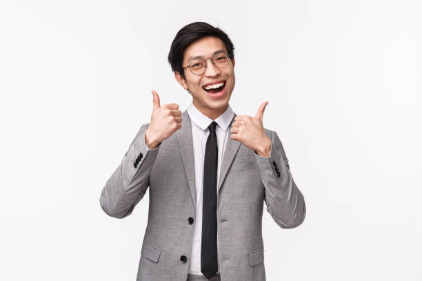 taille-up-porträt von fröhlichen, glücklich und zuversichtlich junge asiatische stattliche geschäftsmann im grauen anzug, zeigt daumen-up und nicken in übereinstimmung, lächelnd genehmigen und wie genial produkt, weißer hintergrund - waistup stock-fotos und bilder