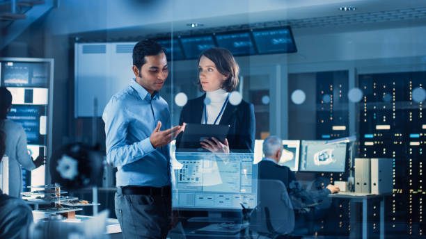 istock In Technology Research Facility: Female Project Manager Talks With Chief Engineer, they Consult Tablet Computer. Team of Industrial Engineers, Developers Work on Engine Design Using Computers 1214111336