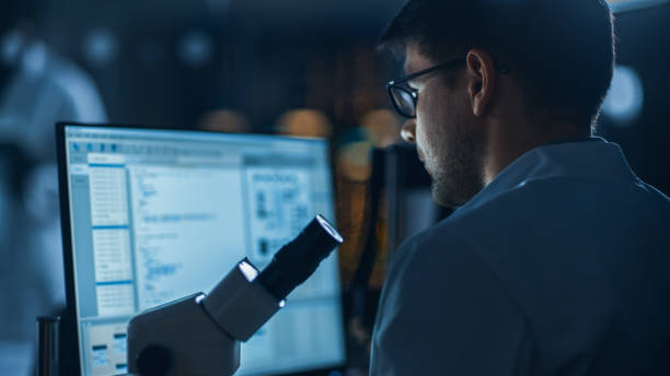 istock Shot of a Male IT Scientist Uses Computer Showing System Monitoring and Controlling Program. In the Background Technology Development Laboratory with Scientists, Engineers Working 1214111342