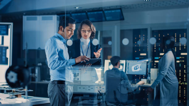 istock In Technology Research Facility: Female Project Manager Talks With Chief Engineer, they Consult Tablet Computer. Team of Industrial Engineers, Developers Work on Engine Design Using Computers 1214111364