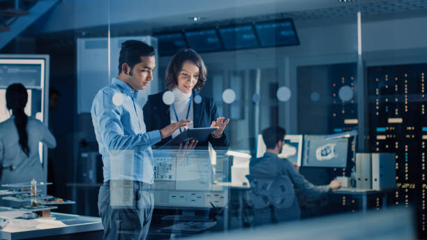 dans le cadre de l’installation de recherche technologique : une femme chef de projet discute avec l’ingénieur en chef, ils consultent tablet computer. équipe d’ingénieurs industriels, développeurs de travail sur la conception de moteur à l’ai - technicien photos et images de collection