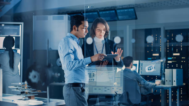 istock In Technology Research Facility: Female Project Manager Talks With Chief Engineer, they Consult Tablet Computer. Team of Industrial Engineers, Developers Work on Engine Design Using Computers 1214111374