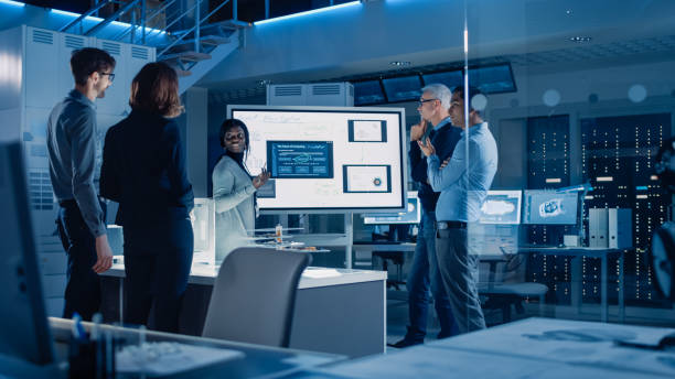 istock Engineers Meeting in Technology Research Laboratory: Male Engineer Leads Presentation Using Digital Whiteboard, Shows Machine Blueprint, Data Analytics and Neural Network while Colleagues Listening 1214111391