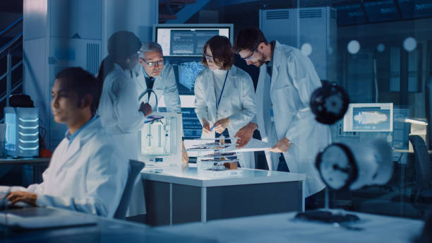 istock In Technology Research Laboratory: Diverse Team of Industrial Scientists, Engineers, Developers Work with Digital Whiteboard Showing Engine Blueprints, Efficiency Calculated by Neural Network 1214111430