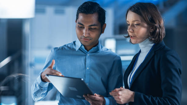 istock In Technology Research Facility: Female Project Manager Talks With Chief Engineer, they Consult Tablet Computer. Team of Industrial Engineers, Developers Work on Engine Design Using Computers 1214111489