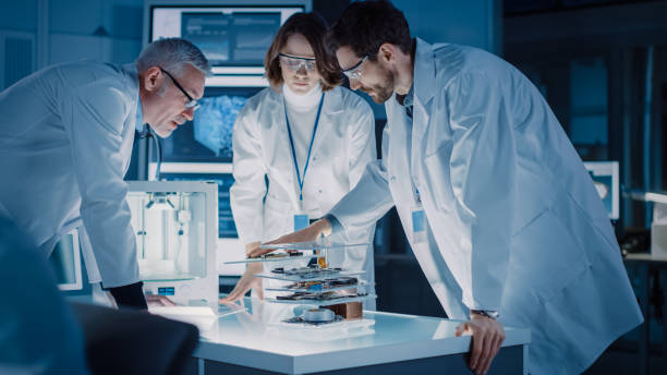 istock Shot in Industrial Design Laboratory, Specialist Uses Microscope, Designer Works on Personal Computer, Researcher Writes on Glass Whiteboard, Team of Developers Use 3D Printer and Motherboard 1214112013