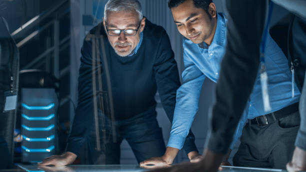 istock Engineers Meeting in Technology Research Laboratory: Engineers, Scientists and Developers Gathered Around Illuminated Conference Table, Talking and Finding Solution, Inspecting and Analysing Industrial Engine Design. 1214112026