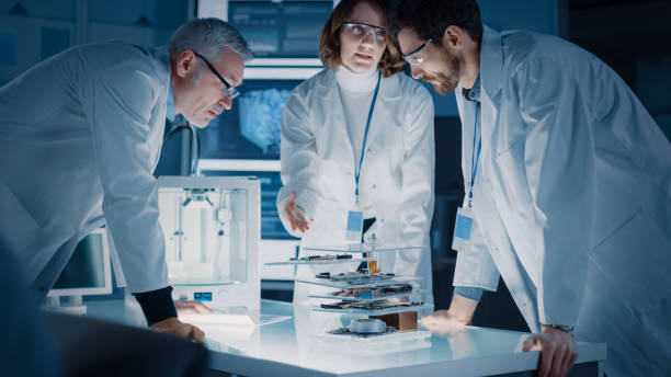 istock Shot in Industrial Design Laboratory, Specialist Uses Microscope, Designer Works on Personal Computer, Researcher Writes on Glass Whiteboard, Team of Developers Use 3D Printer and Motherboard 1214112046