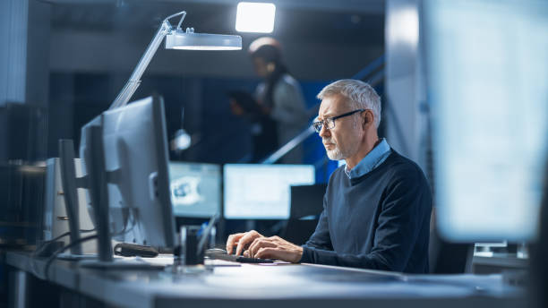 istock Shot of Industrial Engineer Working in Research Laboratory / Development Center, Using Computer. In the Background Technology Development Laboratory with Scientists, Engineers Working 1214112096