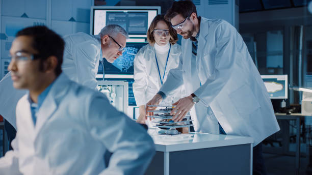 istock Shot in Industrial Design Laboratory, Specialist Uses Microscope, Designer Works on Personal Computer, Researcher Writes on Glass Whiteboard, Team of Developers Use 3D Printer and Motherboard 1214112122