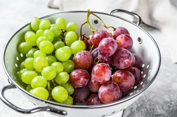 Photo of Two varieties of grapes, red and green in a colander. Gray background. Top view