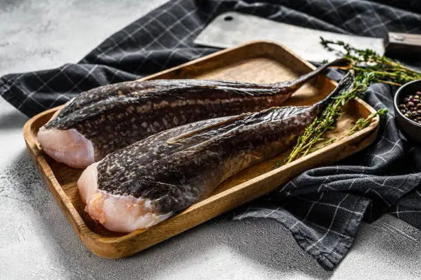 Fresh monkfish without a head on a wooden tray with a cleaver. Gray background. Top view.