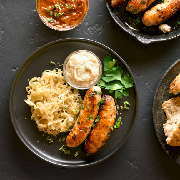 Grilled sausages Grilled sausages with sauerkraut and horseradish on plate over black stone background. Top view, flat lay oktoberfest food stock pictures, royalty-free photos & images