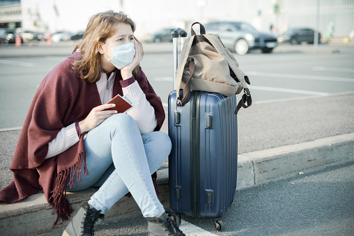 Young woman wearing medical mask, with a suitcase