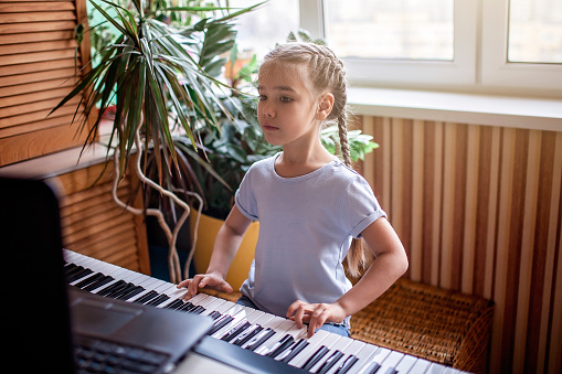 Pretty young musician playing classic digital piano at home during online class at home, social distance during quarantine, self-isolation, online education concept