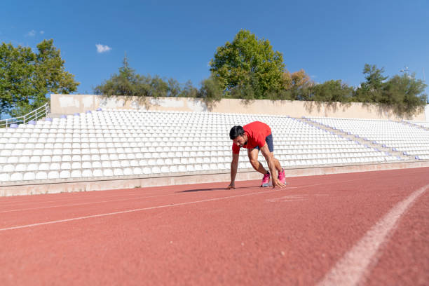 Runner using starting block to start his run on race track. Runner using starting block to start his run on running track in a stadium. Athlete starting his sprint on an all-weather running track. corredor usando el bloque de partida para comenzar su carrera en la pista de carreras. corredor usando el bloque de salida para comenzar su carrera en pista de atletismo en un estadio. atleta comenzando su sprint en una pista de atletismo para todo tipo de