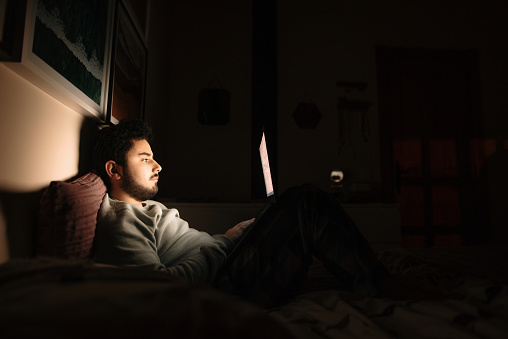 A young man in bed using his laptop