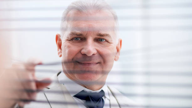 istock close up. smiling businessman looking through window blinds. 1214124317