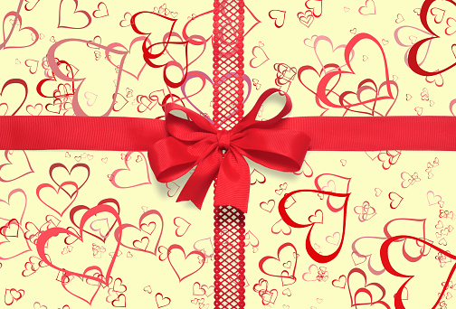 Red gift ribbon with a bow on yellow background with hearts