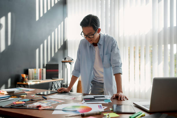 istock Satisfied with my work. Happy asian man in eyeglasses analyzing new design project and smiling while standing in the modern office 1214127403