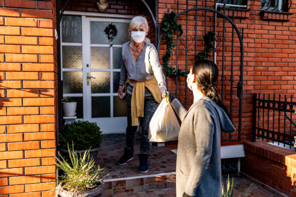 volontaria che porta generi alimentari a una donna anziana a casa - fence mask foto e immagini stock