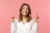 Close-up portrait of hopeful, optimistic attractive woman in white dress, bite lip and smiling as daydreaming, hope dream come true, making wish or praying, standing pink background
