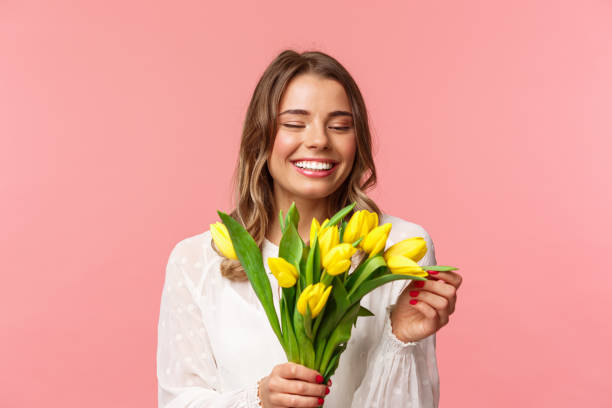 frühling, glück und festkonzept. nahaufnahme porträt von schönen romantischen lächelnmädchen berühren blütenblatt von gelben tulpe, halten blumen, erhalten blumenstrauß auf datum, stehend rosa hintergrund - close up beauty in nature flower head flower stock-fotos und bilder