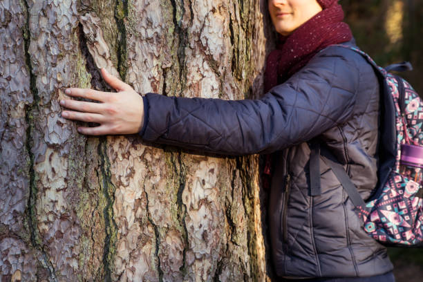 istock Close up calm and smiling young Nature-Lover man with backpack Hugging a Huge Tree Trunk at the forest. Focus on hand with blurred cropped Happy Facial Expression. Nature care. Nature care. Copy space 1214132477