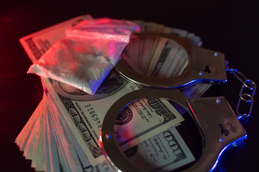 Dólares, esposas, drogas en una mesa en la oscuridad con una luz de luz de la policía roja y azul parpadeando. Concepto de detención, sobornos photo