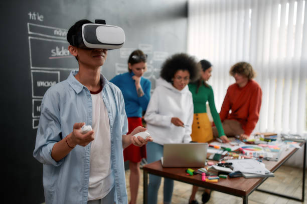 istock Using modern technologies. Young asian man in casual clothes wearing virtual reality glasses while his colleagues discussing new project behind him 1214136084