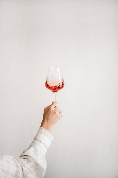 Womans hand holding glass of rose wine Womans hand in white shirt holding glass of rose wine over white wall background. Wine shop, wine tasting, bar, wine list concept sleeve photos stock pictures, royalty-free photos & images