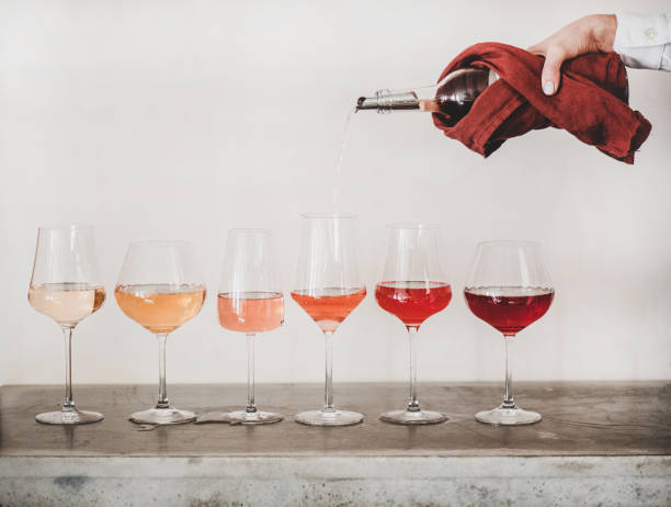 Rose wine shades and womans hand pouring wine to glass Shades of Rose wine in stemmed glasses placed in line from light to deep and womans hand pouring wine from bottle to glass, white wall background behind. Wine bar, wine shop, tasting concept wine tasting stock pictures, royalty-free photos & images