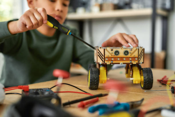 istock Making it better. Close up of a boy using screwdriver while fixing bolts on a robot vehicle. Smart kids and STEM education. 1214139233