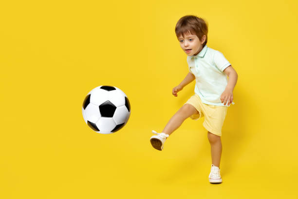 charmantes kleines kind im lässigen sommeroutfit spielen mit fußball über gelbem hintergrund. - soccer child indoors little boys stock-fotos und bilder