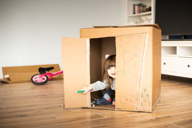 child girl looking out of a cardboard playhouse stock photo