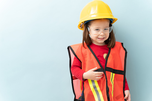 Portrait of a gorgeous little girl dressed up as a construction worker with a helmet and security vest and glasses in a studio